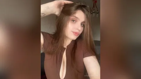 KuvaldaNadin — KuvaldaNadin poses with her hand in her long brown hair while wearing a low-cut brown top.