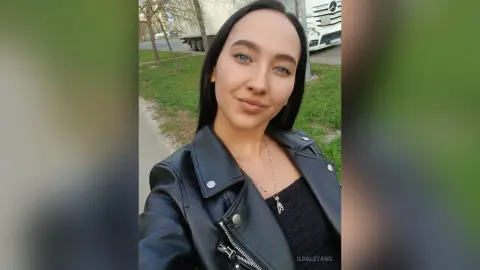 Smiling young woman in a black leather jacket standing outdoors on a sunny day.