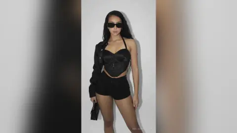Stylish woman in a black corset top, shorts, and sunglasses posing against a minimalist white studio background.