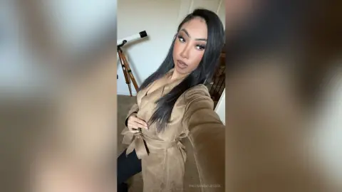 Young woman with long dark hair wearing a stylish tan suede wrap dress in a bright indoor setting.