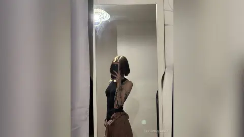 PaulinaCundiff poses for a mirror selfie wearing a black sleeveless bodysuit and brown pants, showing off her arm tattoos.