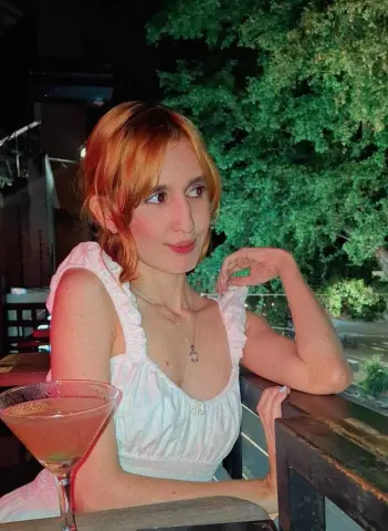 Redheaded woman in a white ruffled sundress sitting at an outdoor cafe terrace at night.