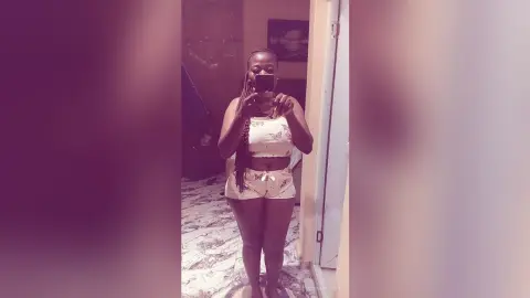 Young woman in white butterfly print lounge set taking a mirror selfie in a cozy bedroom.