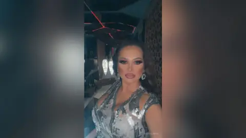 Glamorous woman in a silver sequin cocktail dress posing in a moody, dimly lit lounge setting.