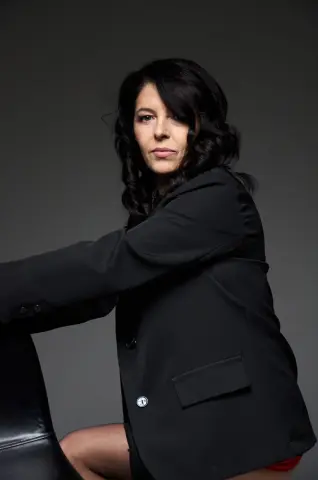Serious brunette woman in a professional black blazer posing against a dark studio background.