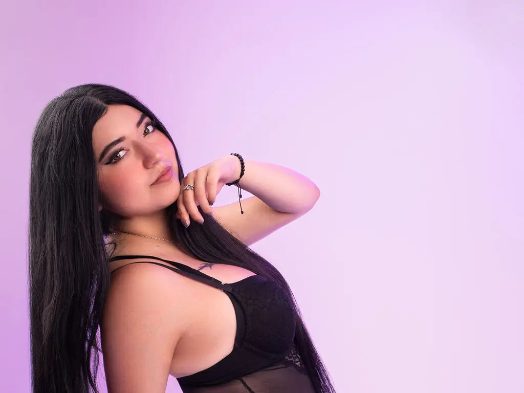 Young woman with long black hair in a black lace bra posing against a soft purple background.