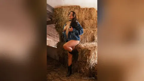 FlorenciaCopper poses naked under an open denim jacket while sitting on a hay bale in a barn.