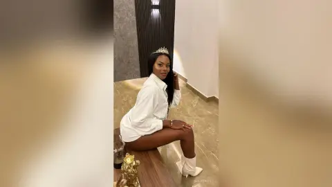 Elegant woman in a white button-down shirt and crown sitting on a floor in a modern luxury interior.