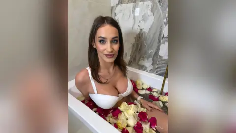 Young woman in white lingerie relaxing in a marble bathtub filled with red and white rose petals.
