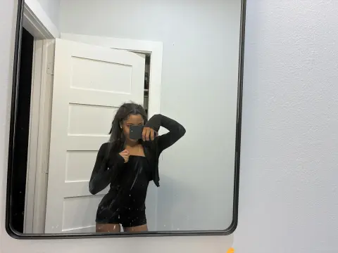 Young woman in a black bodysuit taking a mirror selfie in a bright, modern room.