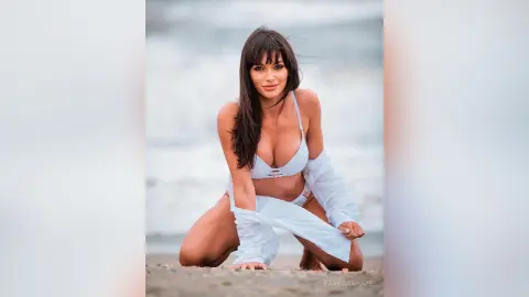 Beautiful woman in a white bikini and open shirt posing on a sunny beach with a serene summer mood.