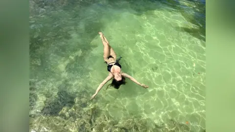 Young woman in a black bikini floating peacefully in clear turquoise tropical ocean water.