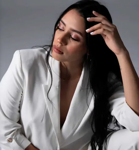 Elegant woman in a white blazer posing with a thoughtful expression against a neutral studio background.