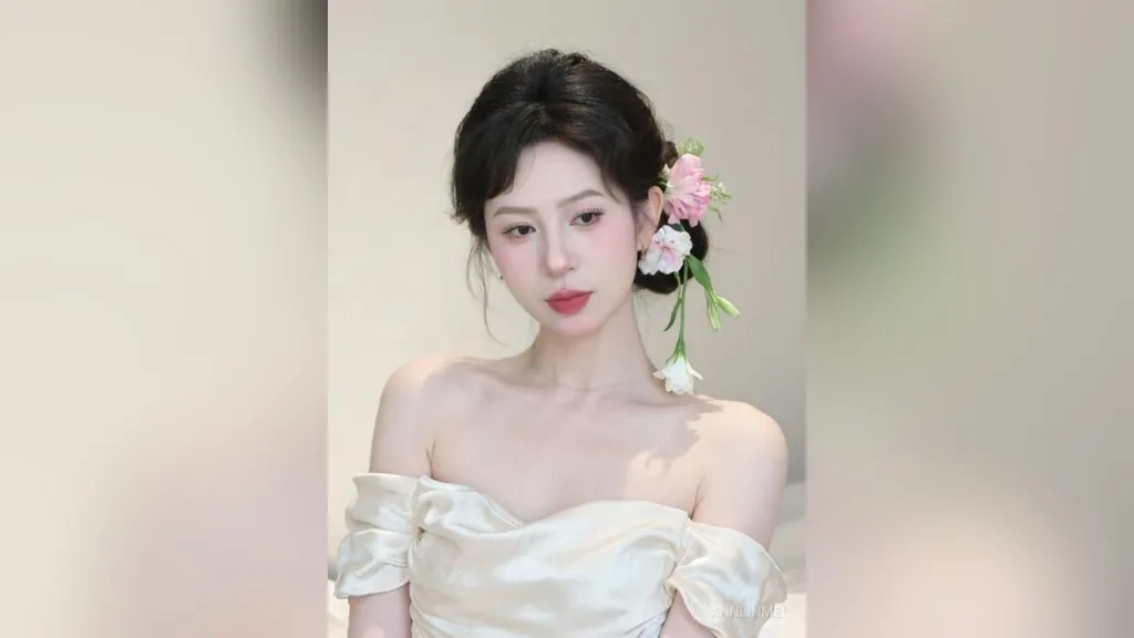 AnnLinMei — AnnLinMei poses in an off-the-shoulder cream satin dress with pink flowers in her dark hair.