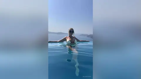 Relaxed woman in white bikini relaxing in a luxury infinity pool overlooking the blue ocean at sunset.