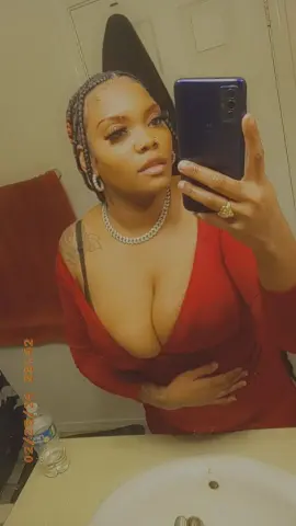Woman in a red V-neck top and silver necklace taking a confident mirror selfie in a bathroom.