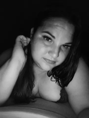 Close-up black and white portrait of a woman with long hair relaxing in a moody, intimate indoor setting.