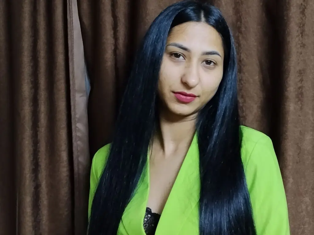 Smiling young woman with long dark hair wearing a bright lime green blazer in a cozy indoor setting.