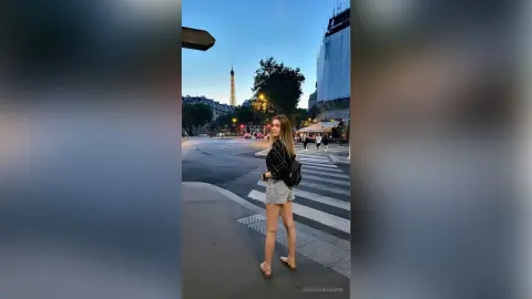 JessicaAidennn — Stylish woman in denim shorts and black shirt walking near the Eiffel Tower in Paris at twilight.