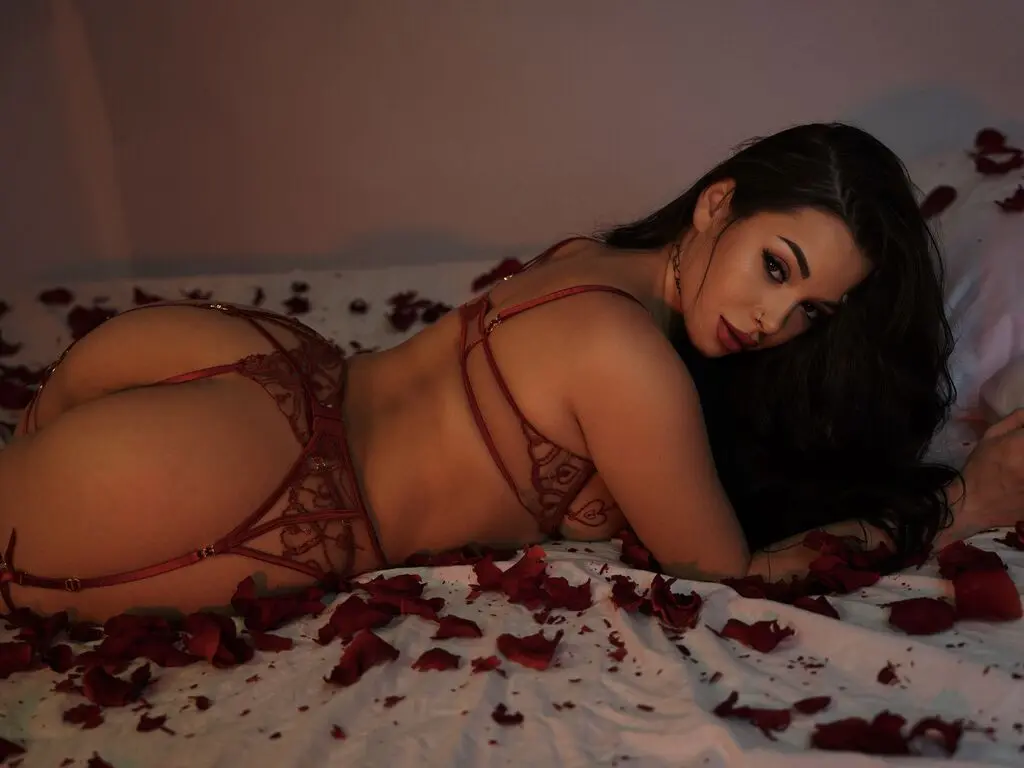 Woman in red lace lingerie lying on a white bed covered in red rose petals in a romantic mood.
