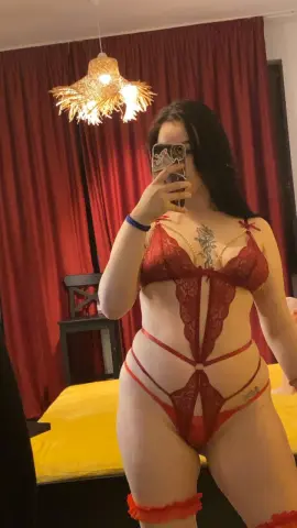 LeahBrookss poses in a red lace teddy and red thigh garters, showing her long dark hair and cleavage in a bedroom setting.