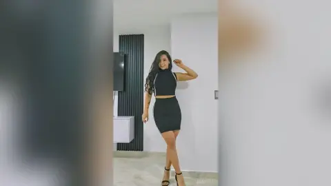 Stylish woman in a black sleeveless crop top and mini skirt posing in a modern minimalist room.