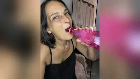 MichaelaBelle sips from a pink bottle while wearing a black tank top and a silver necklace.