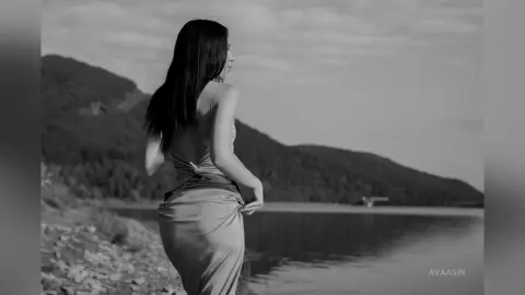AvaaSin stands by a lake, wearing a low-cut backless dress that drapes over her hips.