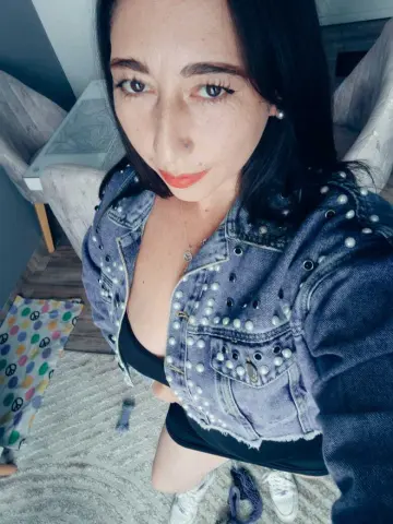 Woman in a studded denim jacket and black top posing indoors with a casual, confident mood.