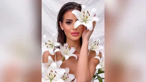 Beautiful woman with long brown hair holding white lilies against a soft white background for a dreamy aesthetic.