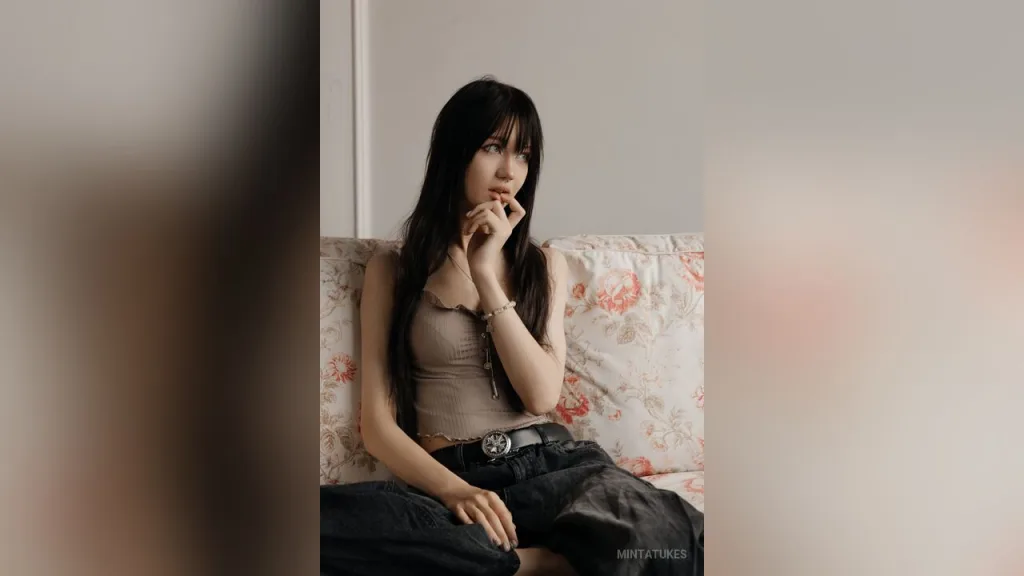 MintaTukes — MintaTukes sits on a floral patterned sofa wearing a tan tank top and black jeans.