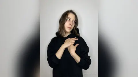 Young woman in a black hoodie looking away thoughtfully against a plain white background.