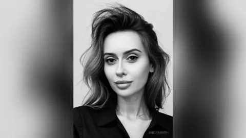 Black and white portrait of a woman with voluminous wavy hair wearing a dark collared shirt in a minimalist setting.