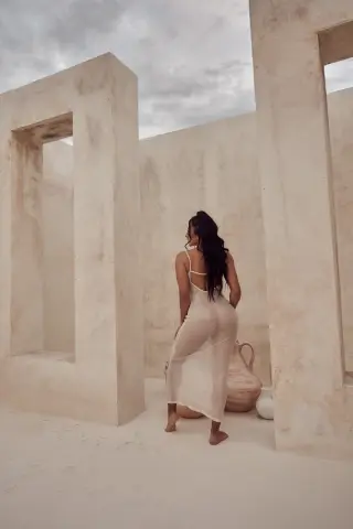 Woman in a white slip dress standing in a minimalist beige stone courtyard under a cloudy sky.