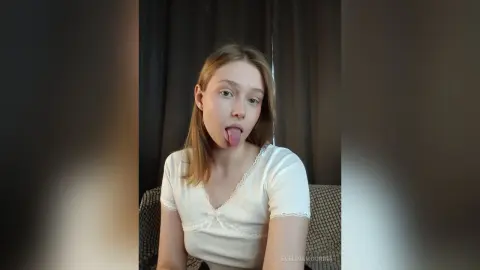 EvelinaMoorina is a blonde woman in a white lace top sticking her tongue out at the camera.
