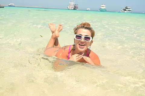 Smiling woman in white sunglasses relaxing in turquoise tropical ocean water on a sunny summer vacation.
