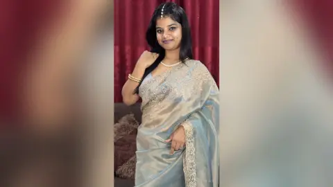 Sejuti poses in a silver silk saree with gold embroidery, wearing a pearl necklace and gold bangles against a red curtain background.