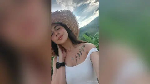 RossiNoleen smiles while wearing a straw hat and a white tank top, showing a leaf tattoo on her shoulder.