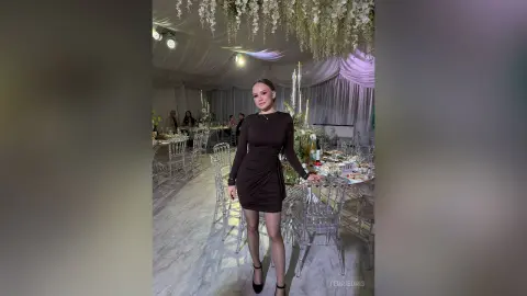 Elegant woman in a black long-sleeve cocktail dress at a glamorous white floral wedding reception.