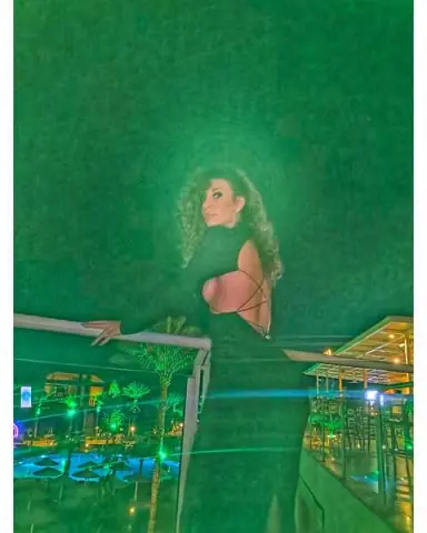 Glamorous woman in a black backless dress posing on a balcony under moody green lighting.