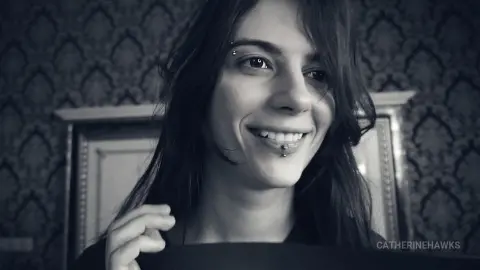 Smiling young woman with dark hair and chin piercing in a moody, vintage-style indoor setting.