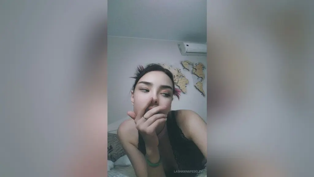 LashawnaPedelty — Young woman in a black tank top looking thoughtful in a bedroom with a world map on the wall.