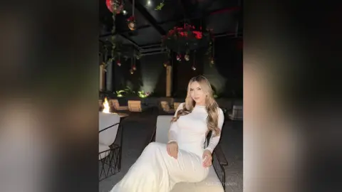 Elegant woman in a white long-sleeve dress sitting at a moody outdoor patio lounge at night.