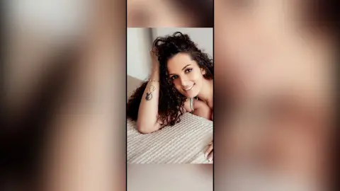 Smiling young woman with curly hair relaxing on a bed in a cozy, intimate indoor setting.