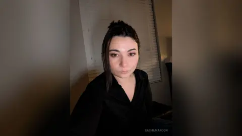 SashaMaroon looks directly at the camera wearing a black button-down shirt with her dark hair styled back.