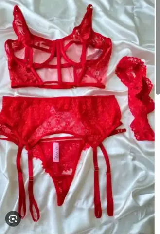 aithna_smitc displays a red lace lingerie set consisting of a sheer bra, garter belt, and matching lace trim laid out on white satin sheets.