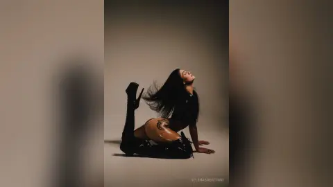 Elegant woman in black bodysuit posing gracefully against a neutral studio background with a moody aesthetic.