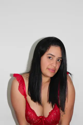 Young woman with long black hair wearing red lace lingerie against a plain white background.