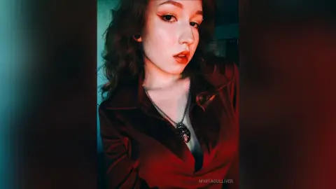 Young woman in a dark red silk blouse and silver necklace posing with a moody, cinematic aesthetic.