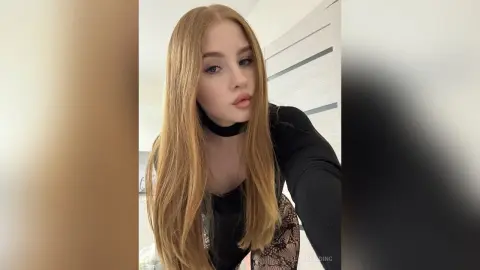 Redheaded woman in a black turtleneck and lace skirt posing in a bright indoor setting with a moody look.